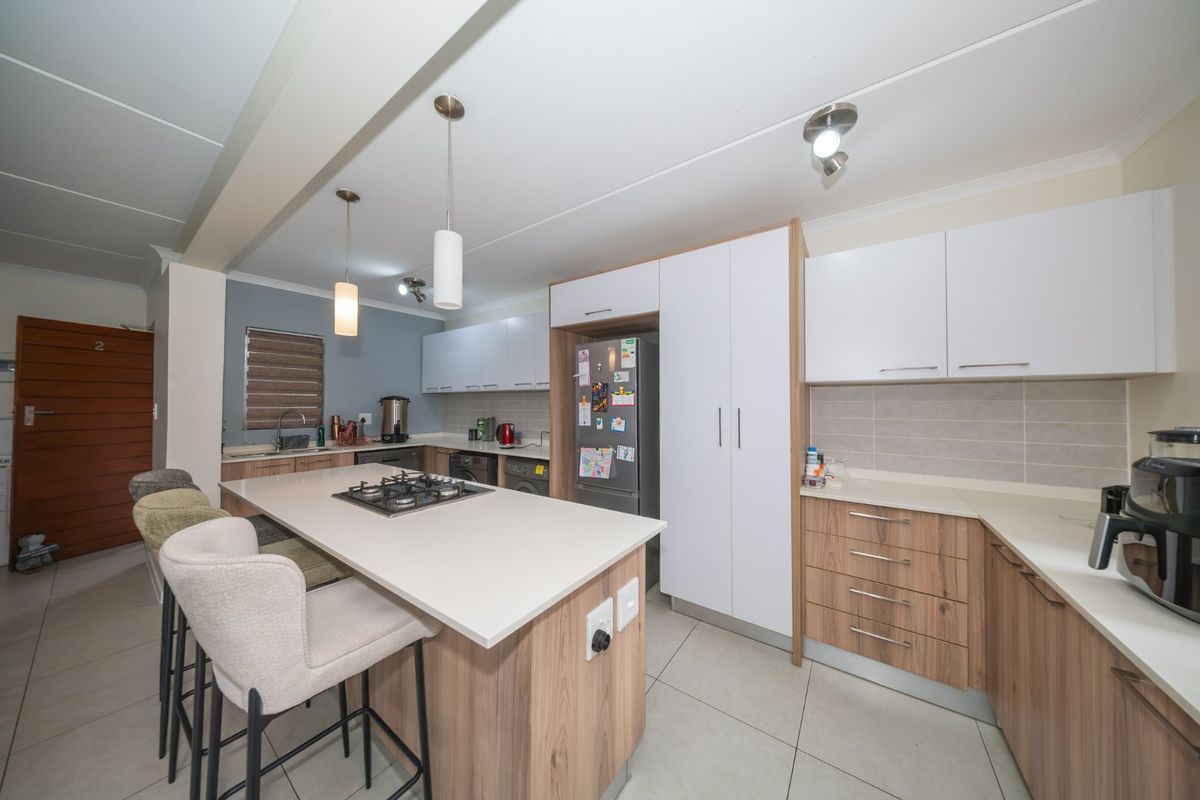 Modern kitchen featuring a central island with a gas hob, ample built-in cabinetry, stone countertops, and neutral tiled flooring.
