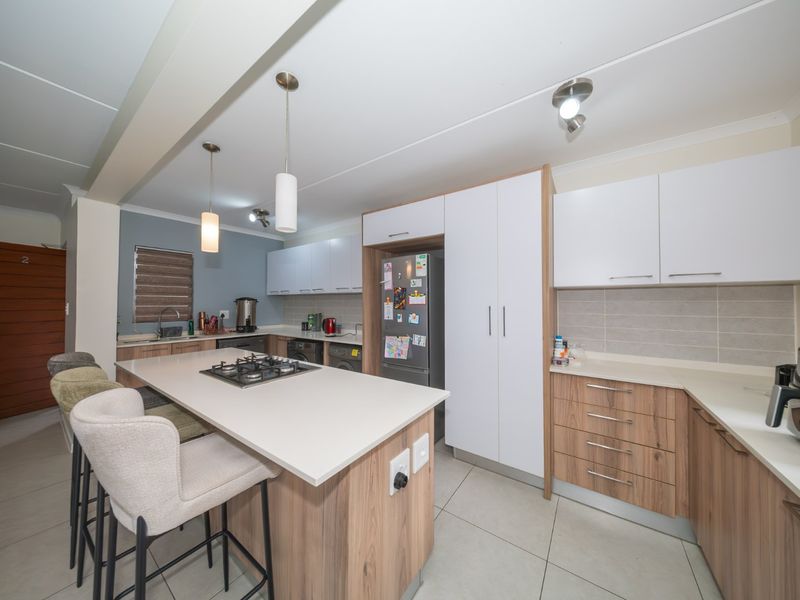 Modern kitchen featuring a central island with a gas hob, ample built-in cabinetry, stone countertops, and neutral tiled flooring.