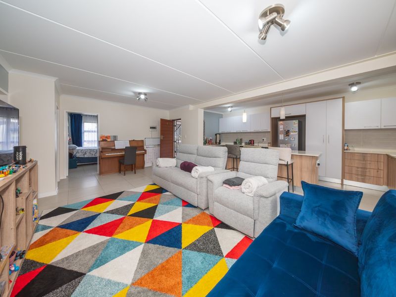 An open-plan living area featuring a modern kitchen with built-in cabinetry, a central island, and tiled flooring, seamlessly connected to the lounge space.