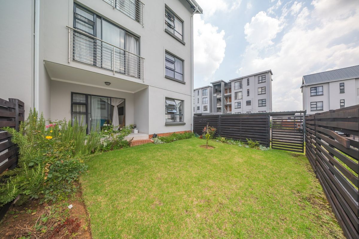 A private rear garden area featuring a small lawn, timber fencing, and a ground-floor patio accessible via sliding glass doors from the townhouse.