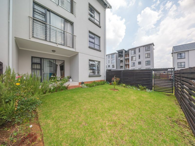 A private rear garden area featuring a small lawn, timber fencing, and a ground-floor patio accessible via sliding glass doors from the townhouse.