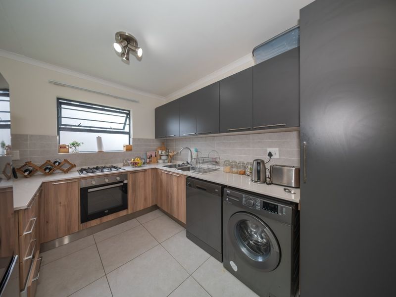 Modern kitchen featuring two-tone cabinetry, stone countertops, gas hob, built-in oven, and integrated laundry appliances, finished with neutral tiled flooring and backsplash.