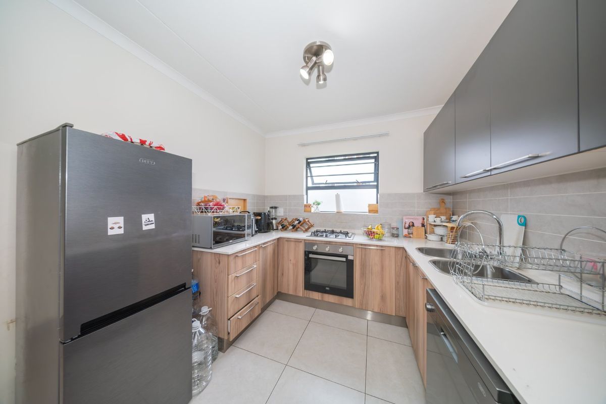 Modern U-shaped kitchen featuring light wood-finish cabinetry, stone countertops, built-in gas hob, oven, and tiled flooring with neutral wall finishes.