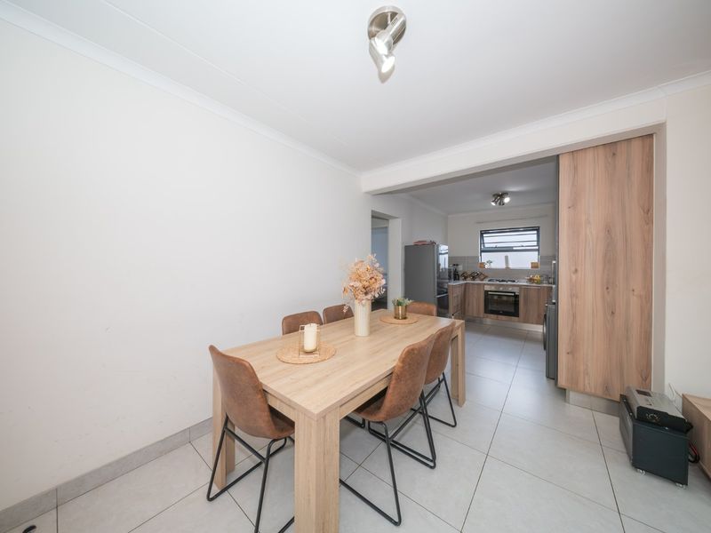 Open-plan dining area flowing into a modern kitchen with wood-finish cabinetry, tiled floors, and built-in cooking appliances.
