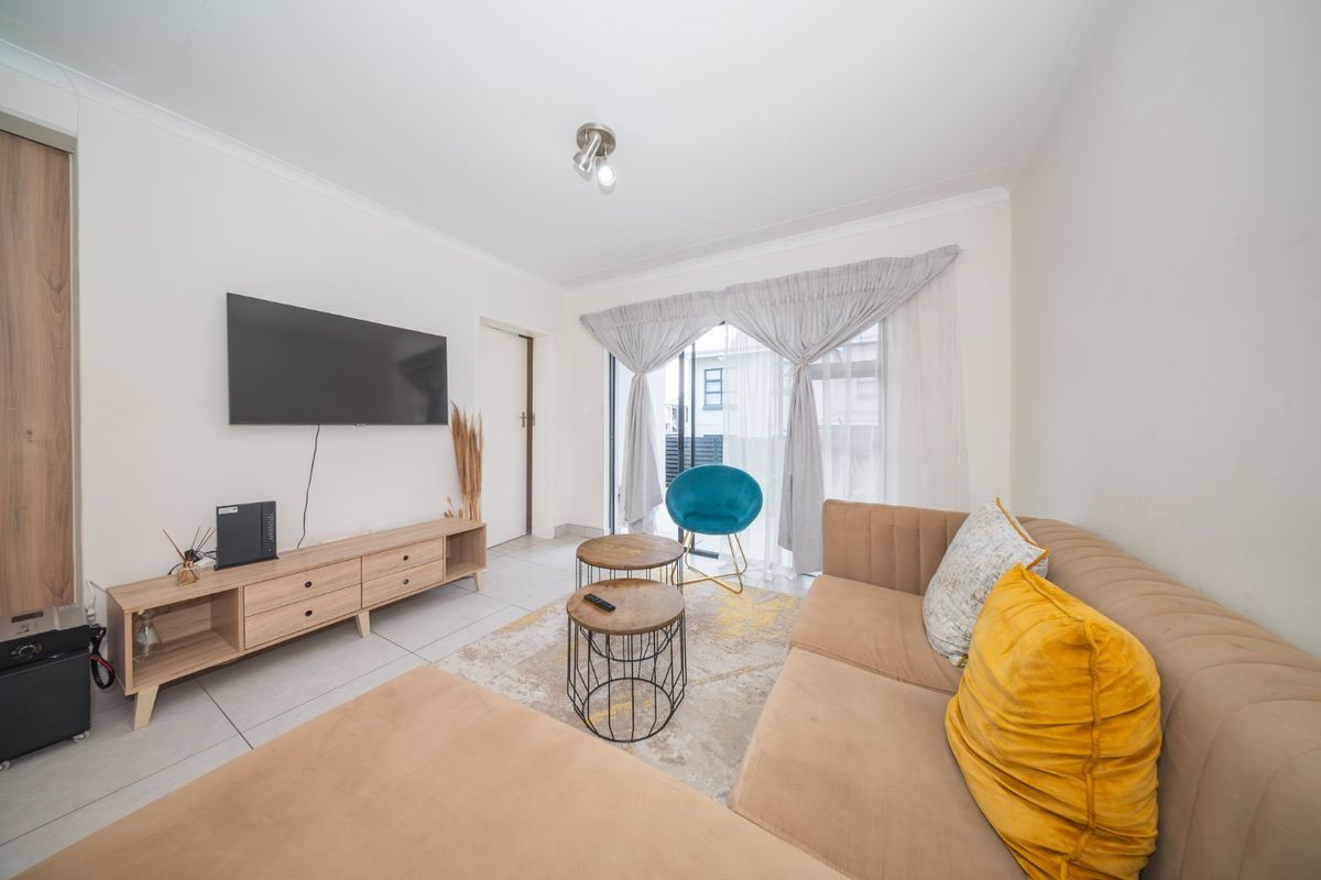 A bright and modern living room featuring tiled flooring and a sliding glass door that provides access to the outdoor area.