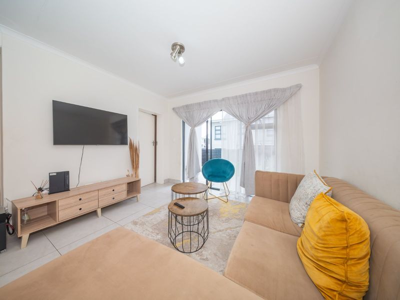 A bright and modern living room featuring tiled flooring and a sliding glass door that provides access to the outdoor area.