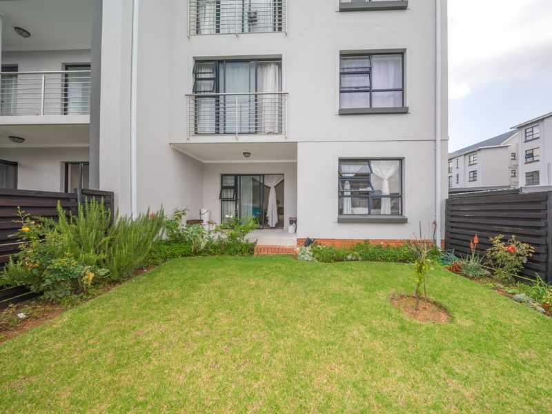 Rear view of a modern townhouse featuring a private garden, timber fencing, and a ground-floor patio with access to upper-level balconies.