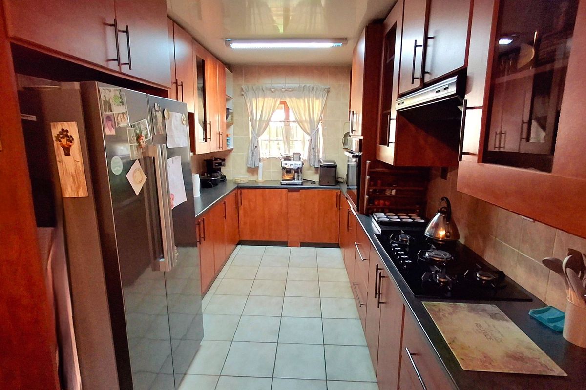 A functional galley-style kitchen featuring wood-finish cabinetry, a gas hob with extractor fan, built-in oven, and tiled flooring.