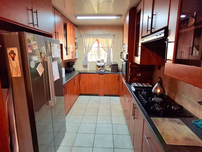 A functional galley-style kitchen featuring wood-finish cabinetry, a gas hob with extractor fan, built-in oven, and tiled flooring.