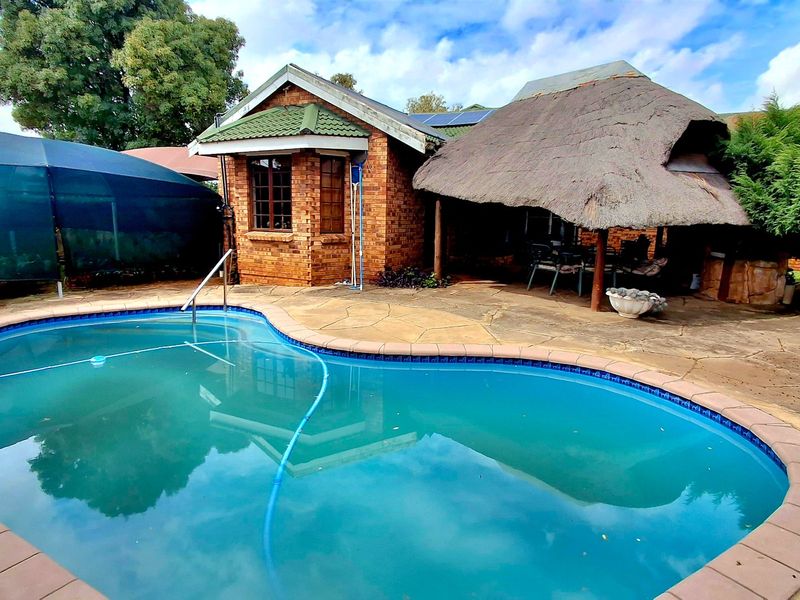 Outdoor pool area featuring a swimming pool, paved patio, and a traditional thatch roof lapa structure.