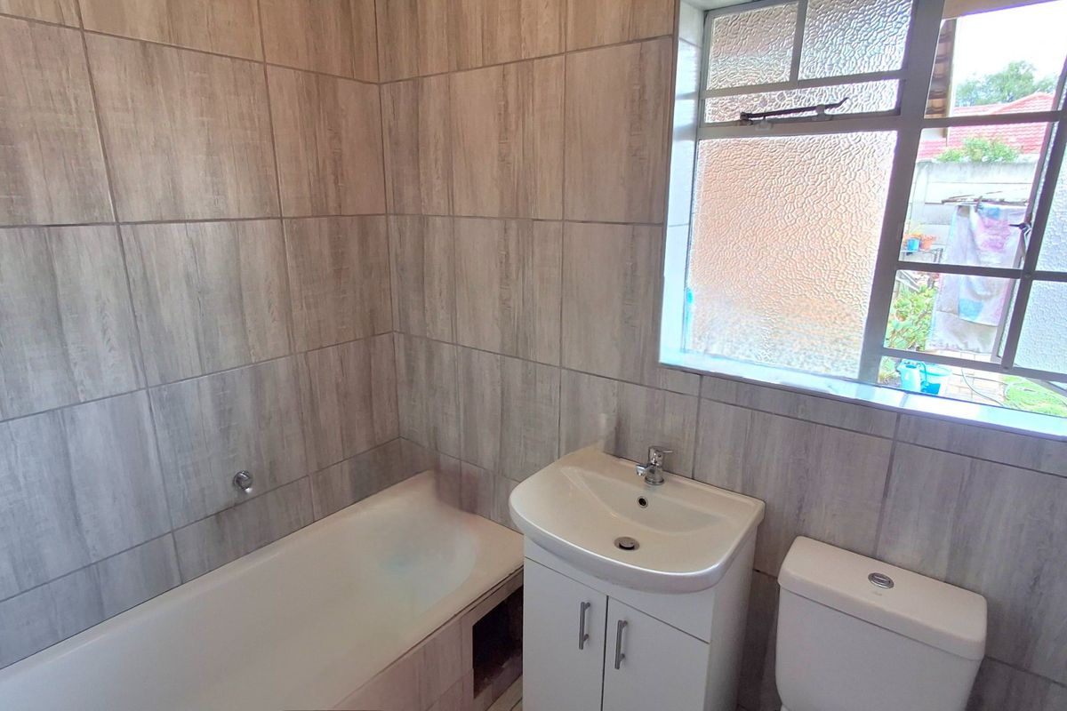 A clean, functional bathroom featuring wood-look wall tiles, a built-in bathtub, a modern vanity unit with a washbasin, and a standard toilet.