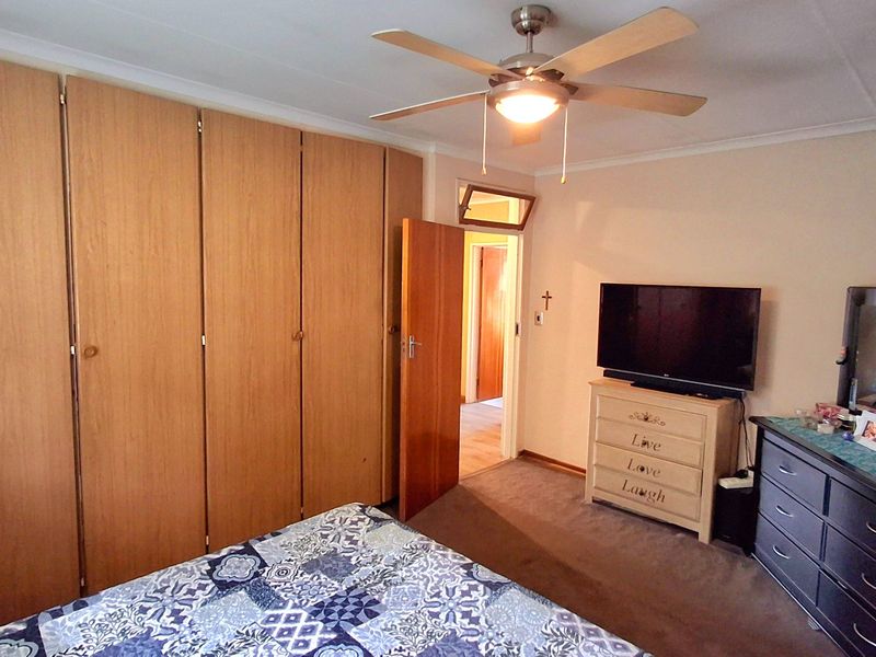 A bedroom featuring built-in wooden cupboards, a ceiling fan, and carpeted flooring, offering a functional and comfortable living space.