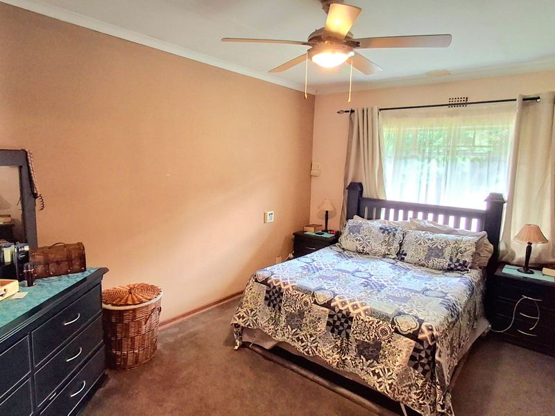 A standard bedroom featuring carpeted flooring, a ceiling fan, and a window with installed curtain rods.