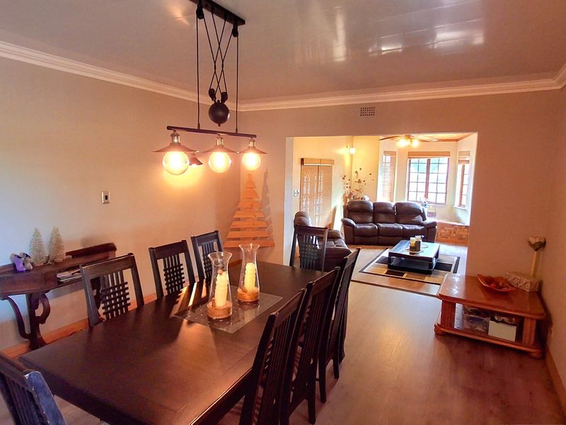 Open plan dining and living area featuring laminate flooring, crown molding, and modern pendant lighting, creating a connected and functional living space.