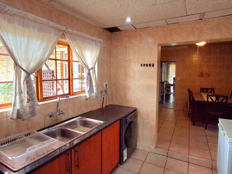Functional kitchen featuring double bowl sink, tiled splashbacks, and built-in cabinetry, with an adjacent dining area visible through the doorway.