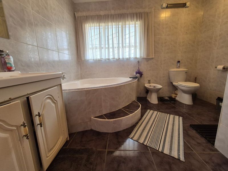 A spacious bathroom featuring a corner bathtub, bidet, toilet, and vanity cabinet with full-height wall tiling.