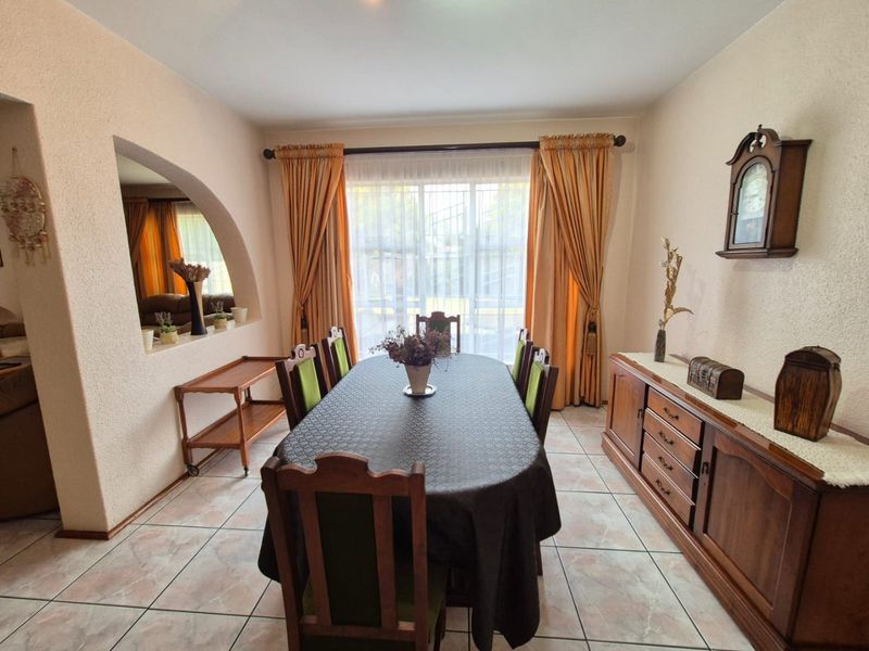 A dining room featuring tiled flooring and a distinctive arched wall opening, providing a view into the adjacent living space.