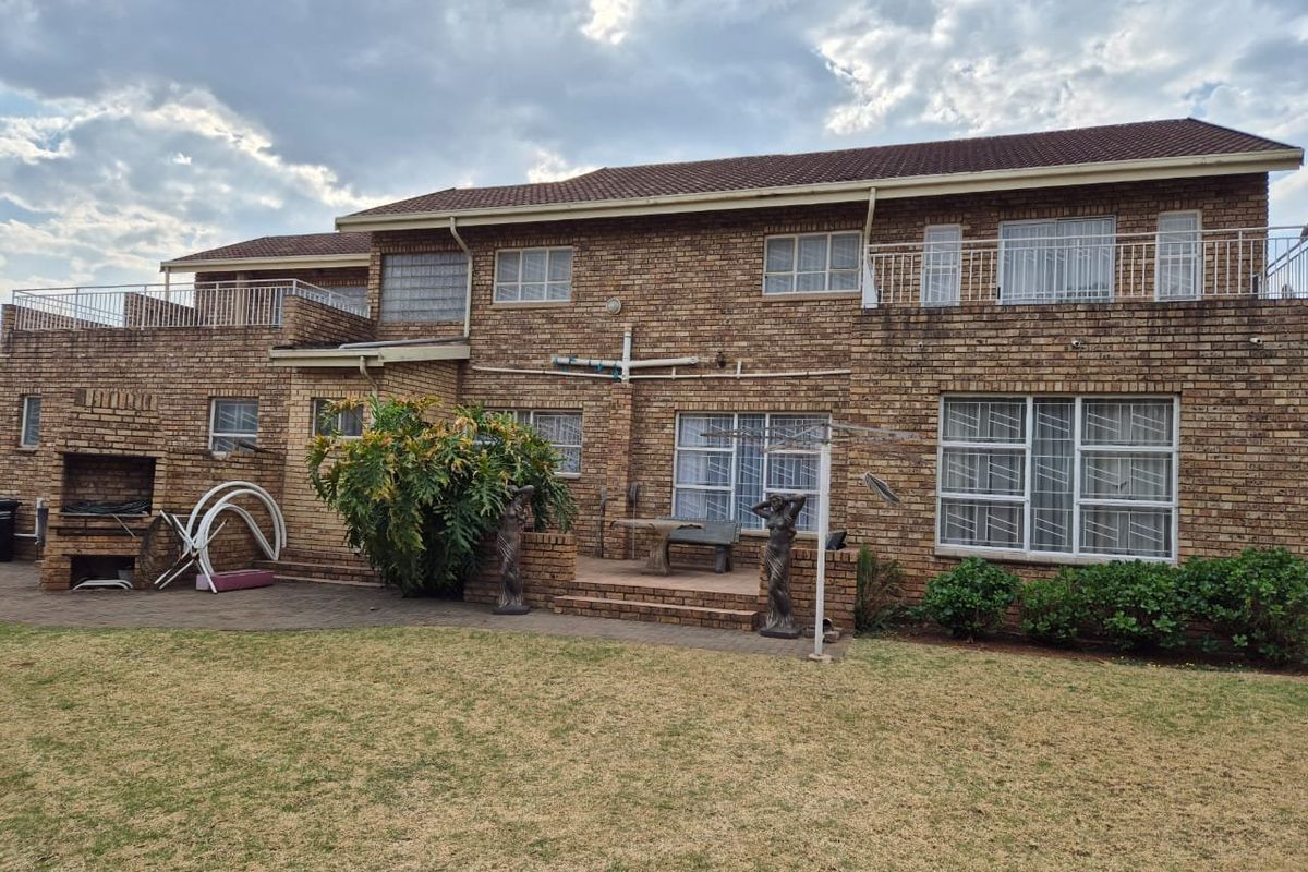 Rear view of a double-storey face brick house featuring a paved patio, built-in braai area, and upper-level balconies overlooking the garden.