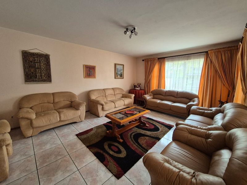A spacious living room featuring neutral tiled flooring and large windows with curtain rails, offering a functional and well-lit living space.
