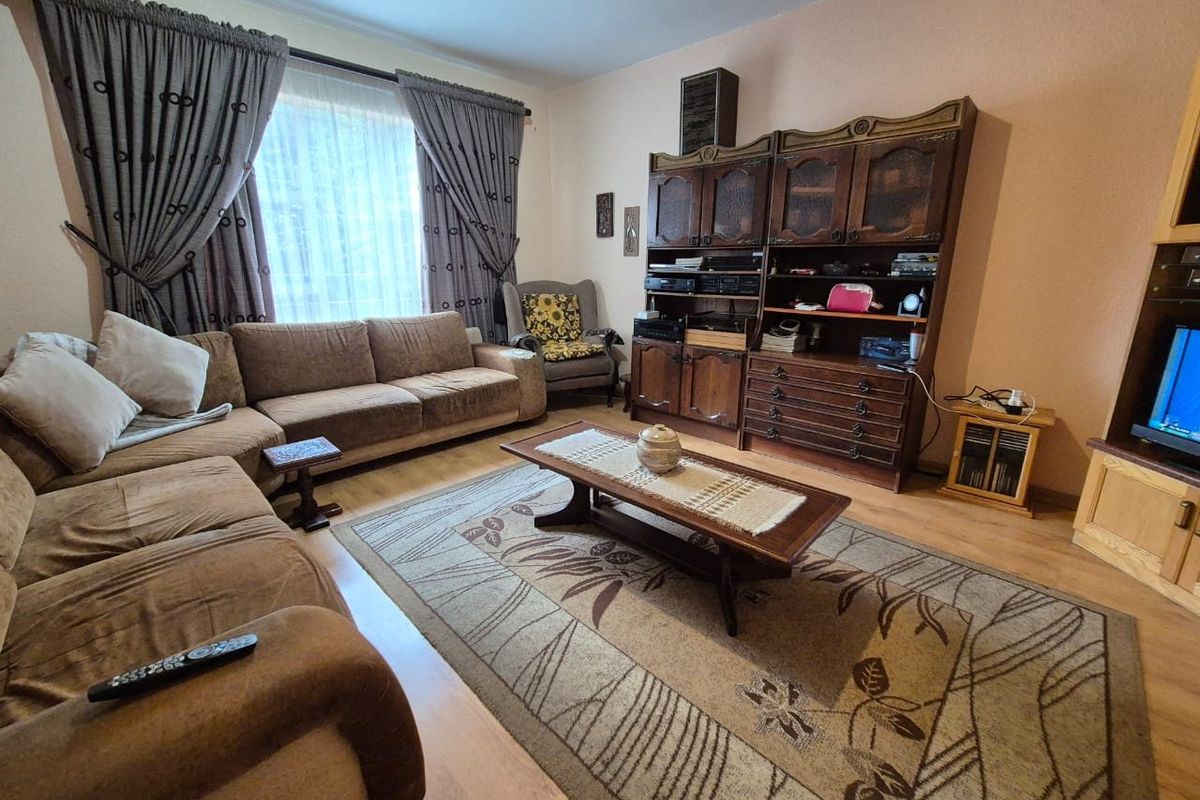 A living room featuring laminate flooring and large windows with curtain treatments, offering a functional space for relaxation.
