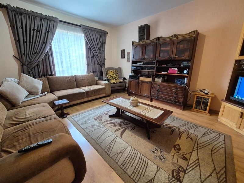 A living room featuring laminate flooring and large windows with curtain treatments, offering a functional space for relaxation.