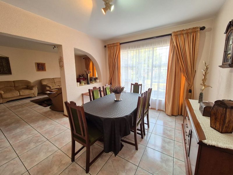 A dining room featuring tiled flooring and a decorative archway connecting to the adjacent living area, with natural light from a large window.