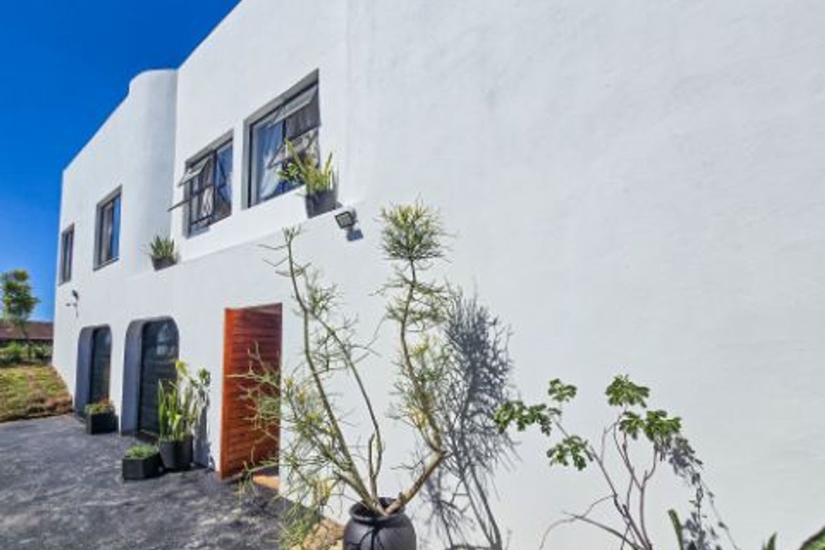 A view of the rear exterior facade featuring white rendered walls, timber door, and casement windows.