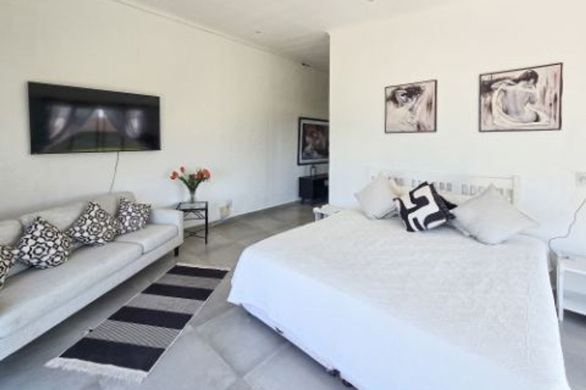 Spacious bedroom featuring neutral tiled flooring and recessed ceiling lighting, offering a versatile layout for a combined sleeping and lounge area.
