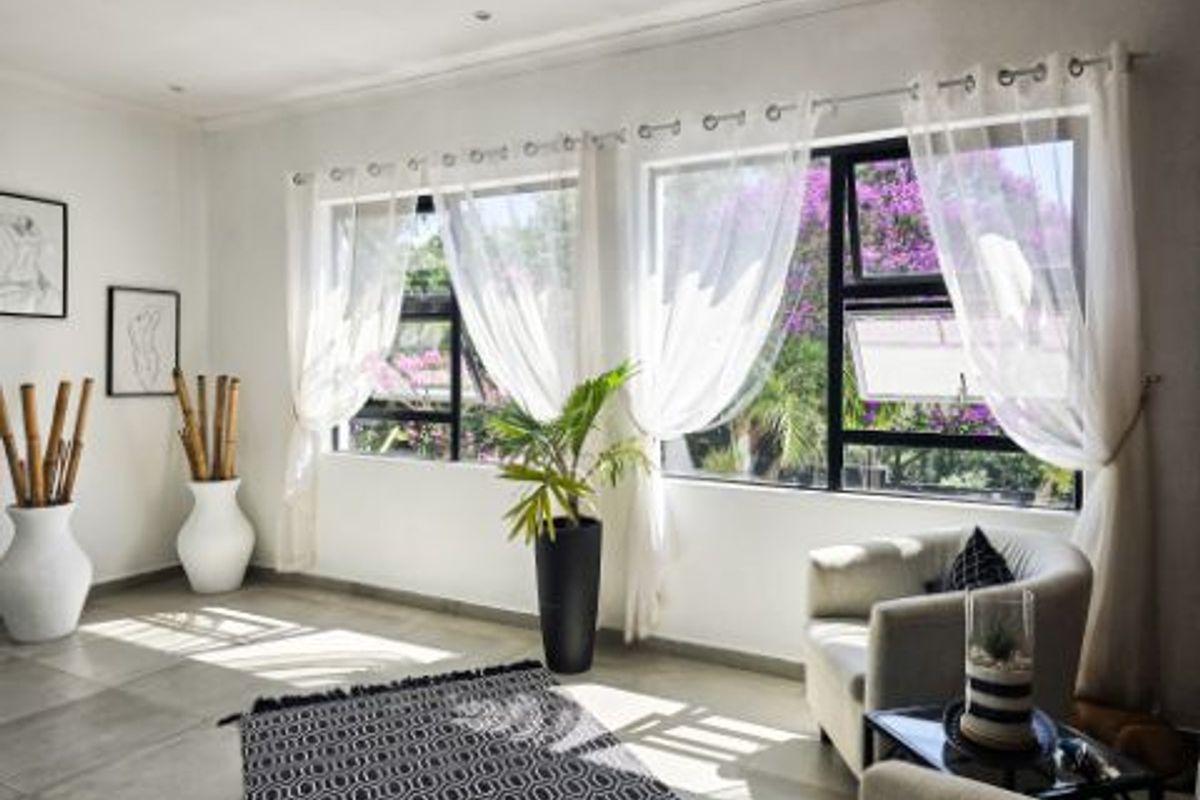 A bright and airy living room featuring large aluminium-framed windows that provide ample natural light and a pleasant garden view.