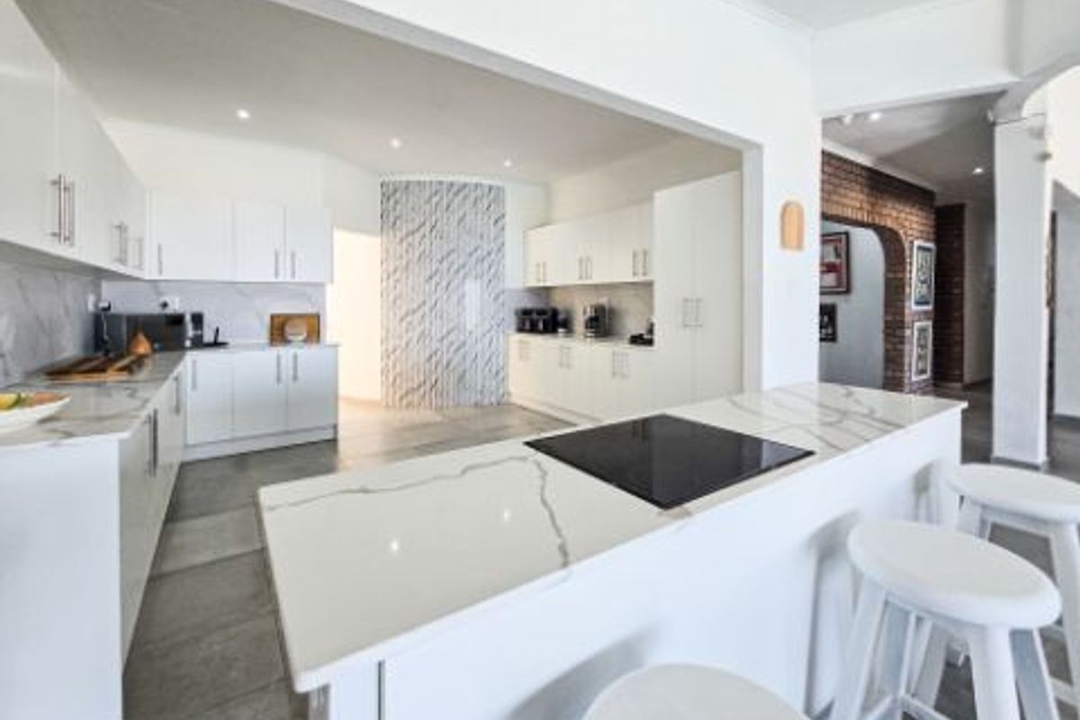 Modern kitchen featuring white cabinetry, stone countertops, a central island with an integrated cooktop, and a decorative tiled feature wall.