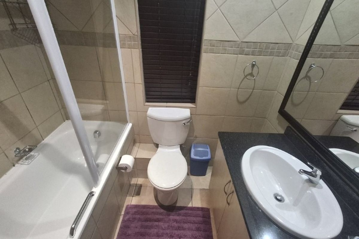 A functional bathroom featuring a bathtub with a glass screen, a vanity with a granite countertop, and tiled finishes throughout.