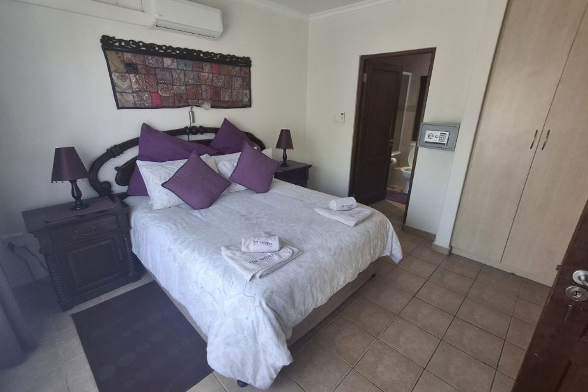 A bedroom featuring tiled flooring, a built-in wardrobe, wall-mounted air conditioning, and an integrated wall safe, with direct access to an en-suite bathroom.