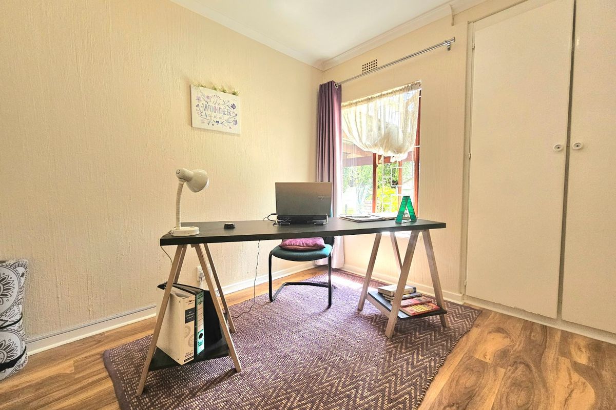 A functional bedroom featuring laminate flooring, recessed downlighting, and a built-in cupboard, currently utilized as a home office space.
