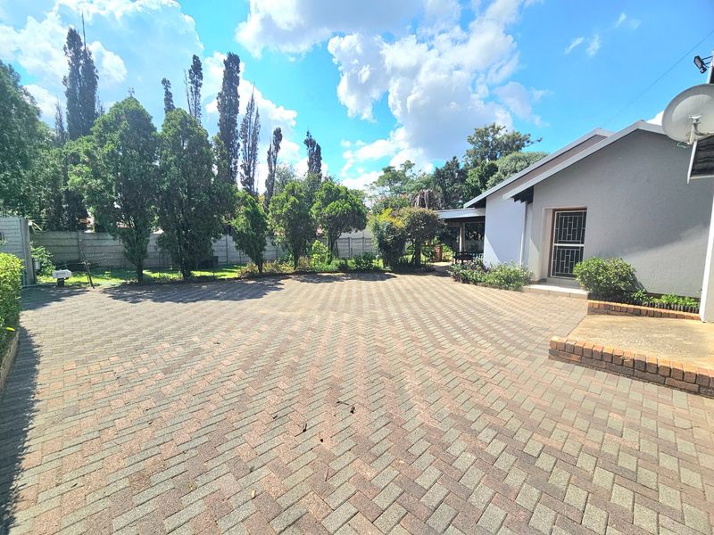 A spacious rear exterior area featuring extensive paved surfacing, a secure entrance, and established garden borders enclosed by a precast concrete boundary wall.