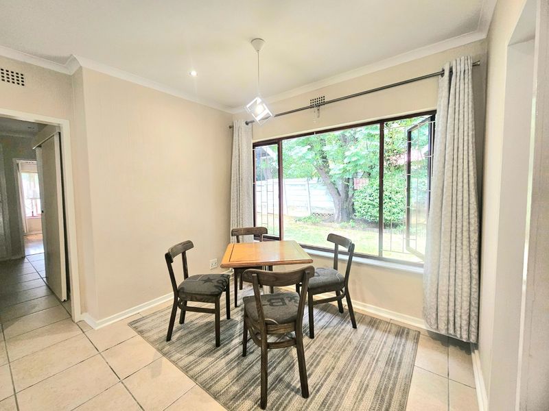 A bright dining area featuring tiled flooring, a large window overlooking the garden, and modern pendant lighting.