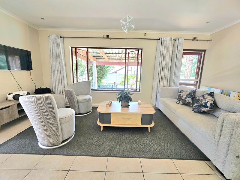 A bright and well-maintained living room featuring tiled flooring, recessed lighting, and large windows that provide natural light and views of the outdoor patio area.