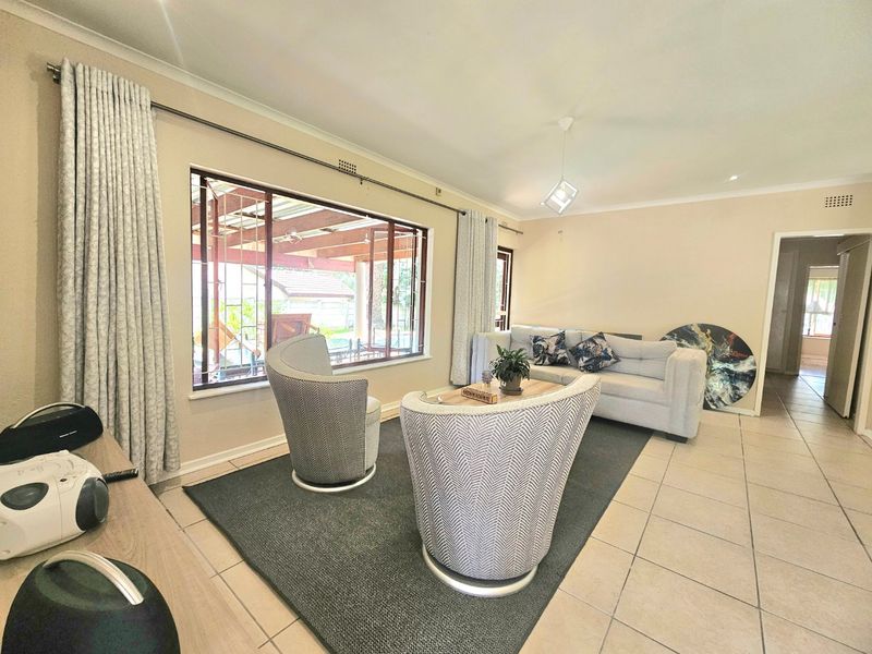 A bright living room featuring neutral ceramic floor tiles, large windows with security bars, and a modern pendant light fixture.