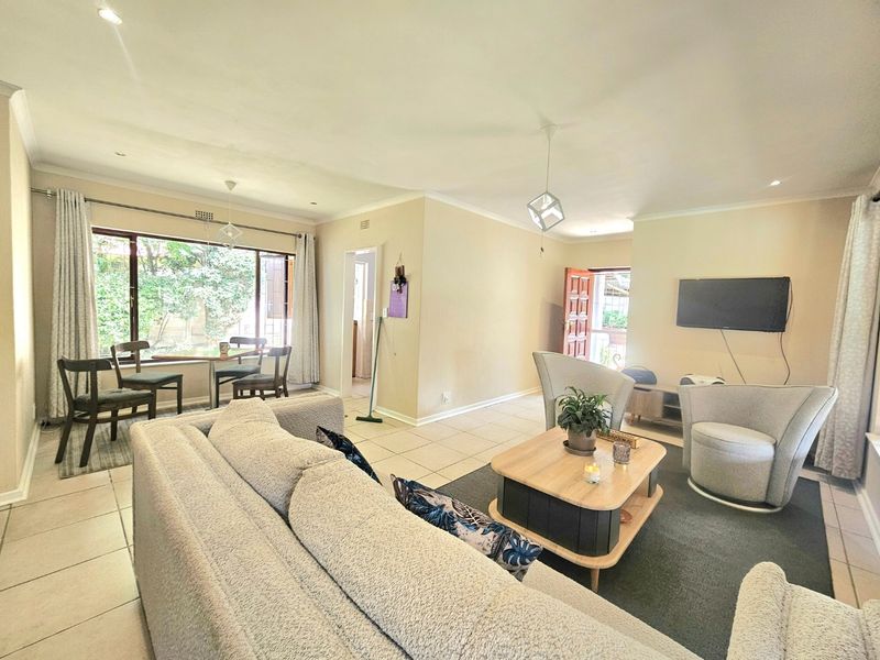 Spacious open-plan living and dining area featuring neutral tiled flooring, recessed downlighting, and large windows providing natural light.