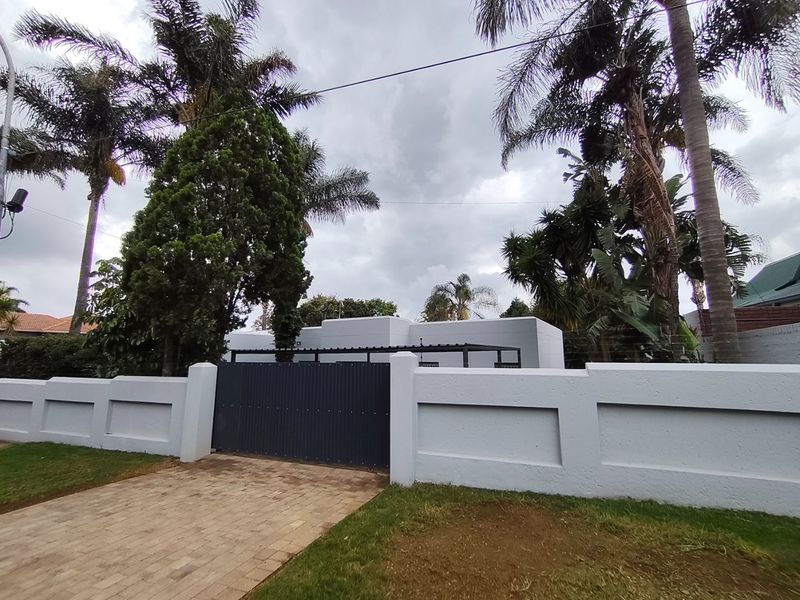 Front view of the property featuring a solid perimeter wall, a modern sliding gate, and a paved driveway entrance.