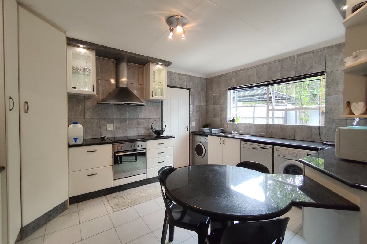 A functional kitchen featuring granite countertops, tiled backsplash, built-in oven with extractor fan, and integrated laundry appliance connections.
