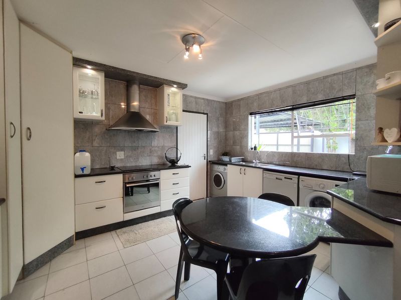 A functional kitchen featuring granite countertops, tiled backsplash, built-in oven with extractor fan, and integrated laundry appliance connections.
