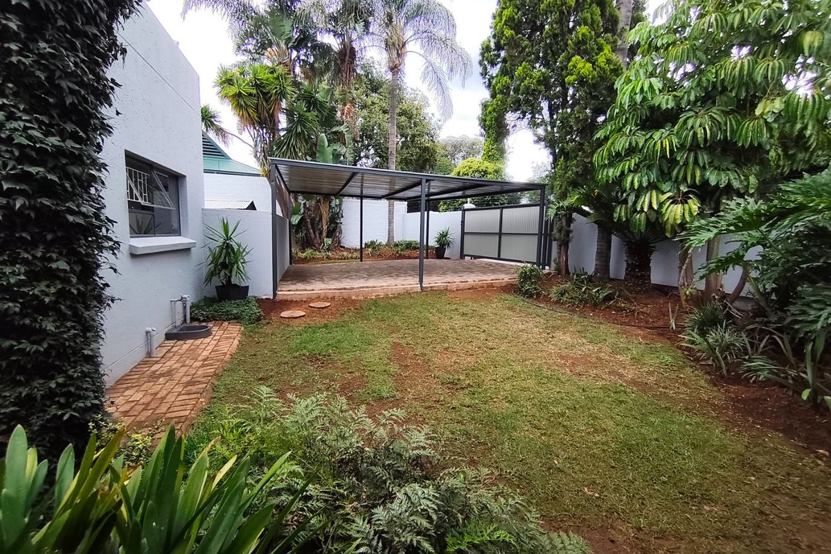 A well-maintained rear garden featuring a covered patio area with paved flooring, surrounded by established trees and a secure boundary wall.