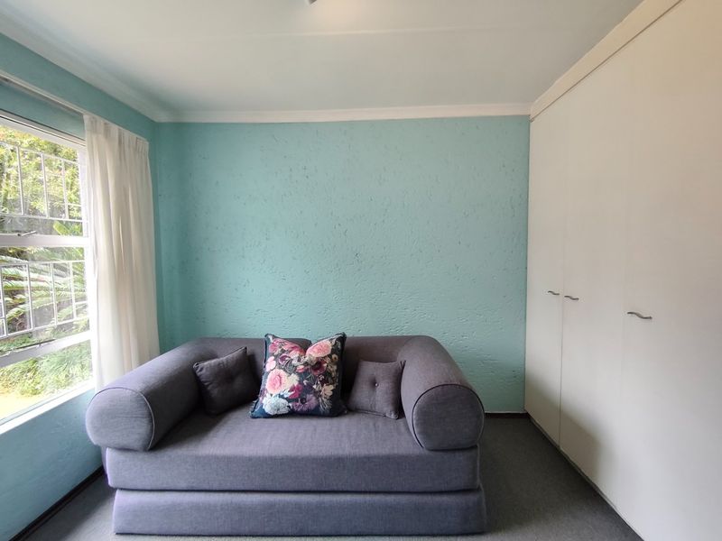 A bedroom featuring built-in cupboards, textured light blue walls, and a large window providing natural light.