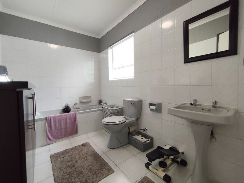 A functional bathroom featuring a built-in bathtub, pedestal washbasin, and toilet with neutral tiled finishes and natural light from a window.