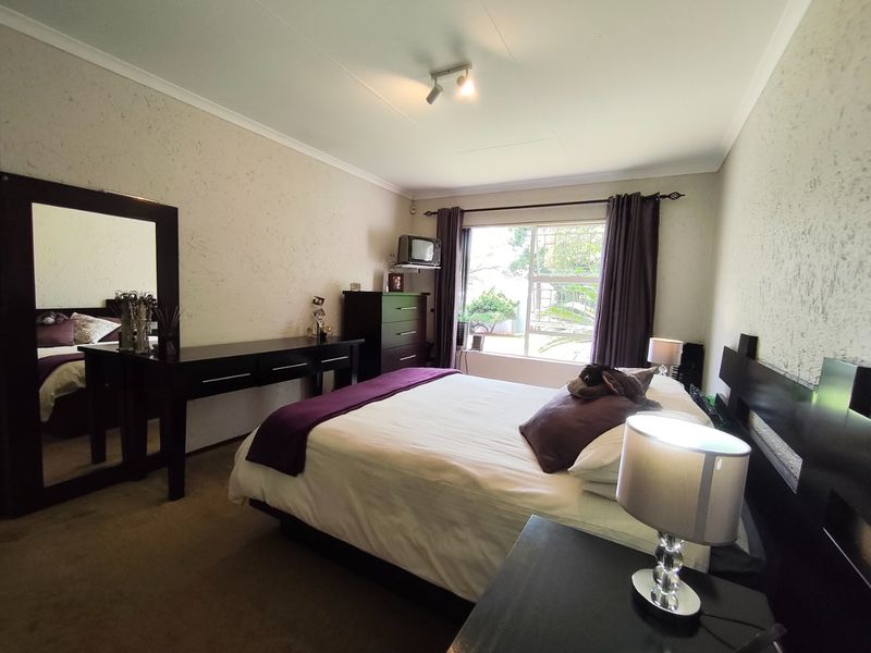 A well-proportioned bedroom featuring carpeted flooring, a window with security bars, and a coved ceiling, offering a comfortable and functional living space.