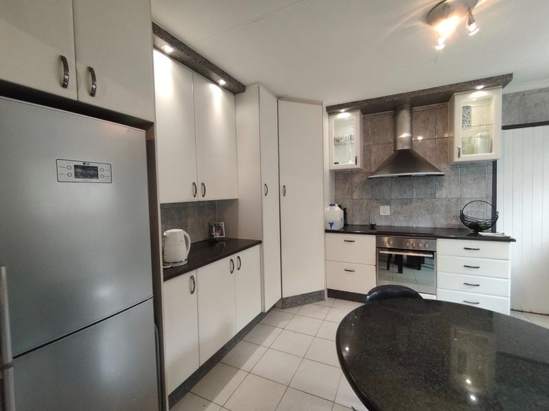 A well-maintained kitchen featuring white cabinetry, granite countertops, a stainless steel extractor fan, built-in oven, and tiled backsplash.