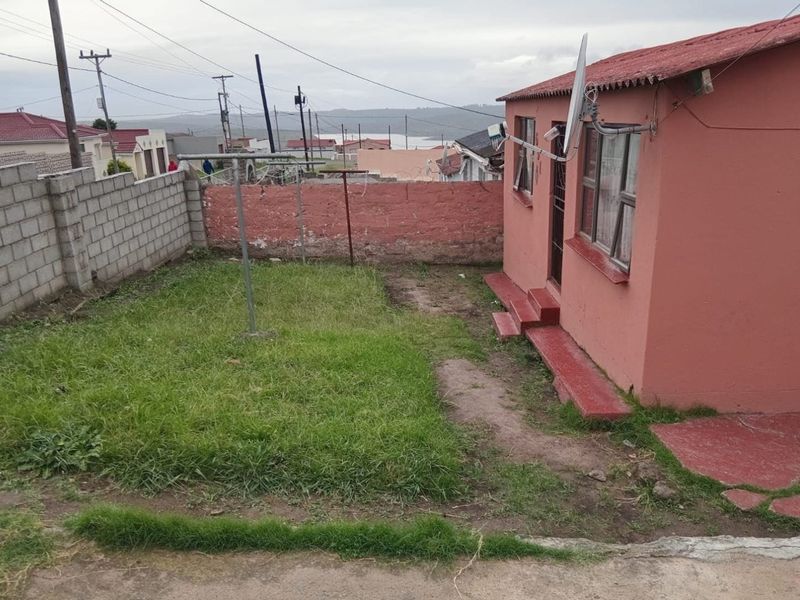 Rear exterior view of the property featuring a small grassed yard, concrete block boundary wall, and painted brick facade.