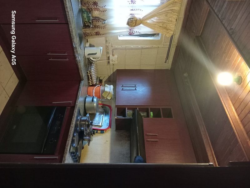 A dated kitchen featuring dark wood cabinetry, built-in oven and hob, and a timber ceiling, requiring cosmetic updates to modernize the space.