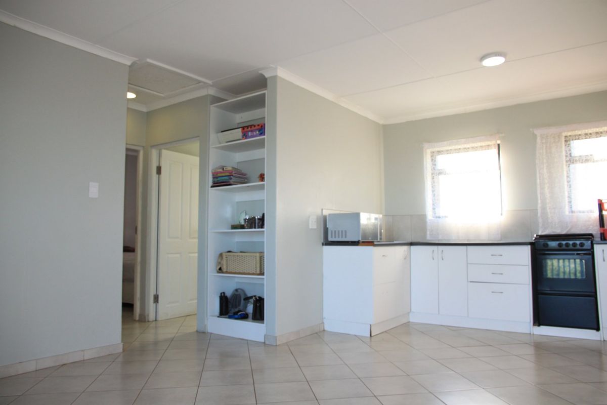 A functional kitchen area featuring white cabinetry, a built-in oven and hob, tiled flooring, and integrated shelving, providing a clean and practical layout.