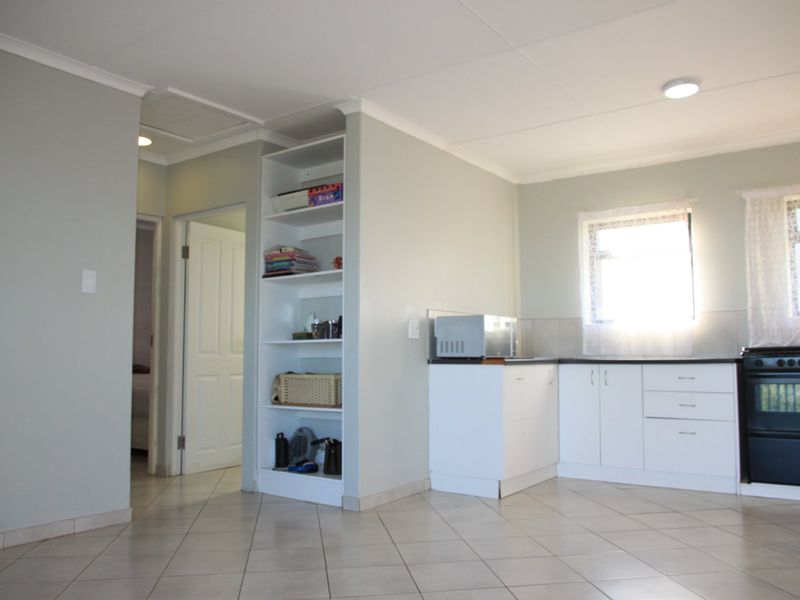 A functional kitchen area featuring white cabinetry, a built-in oven and hob, tiled flooring, and integrated shelving, providing a clean and practical layout.